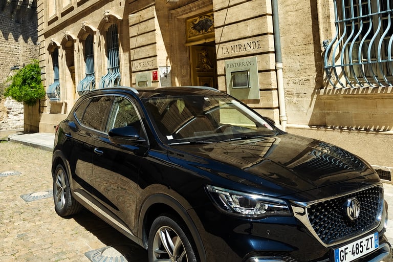 Black MG SUV parked on a cobblestone street in front of La Mirande Hotel in Avignon, France.