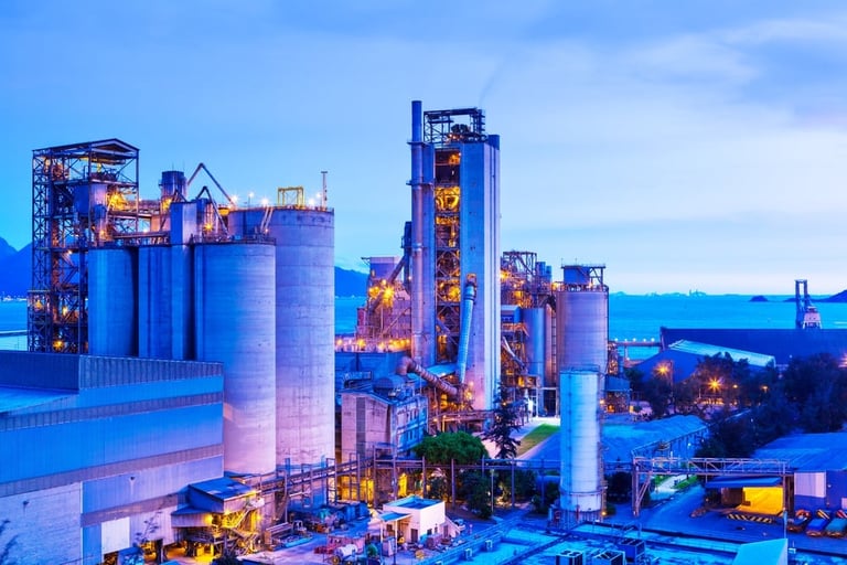 Industrial manufacturing plant with large storage silos and towers illuminated at twilight.