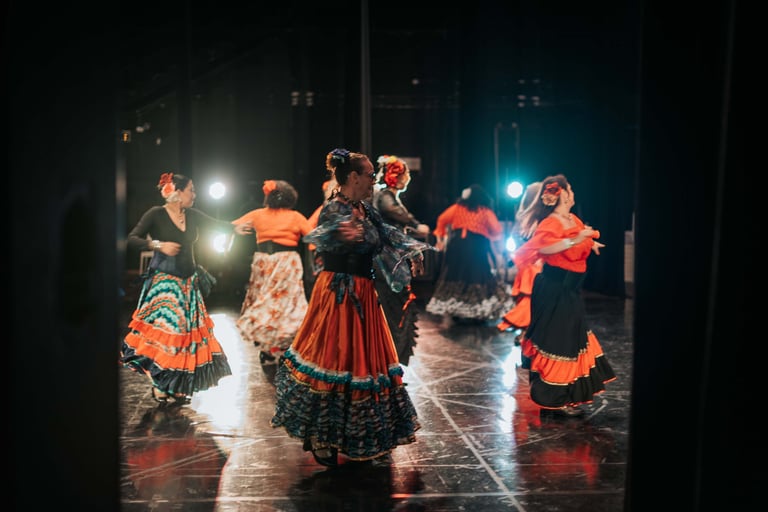 Traditional flamenco dancers performing in colorful ruffled skirts on a theater stage with stage lights.