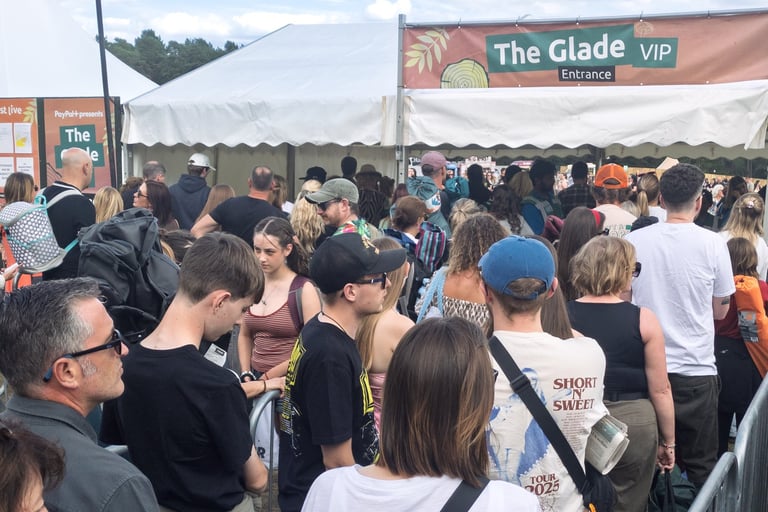 A crowd of people waits in a long queue at the Glade VIP entrance of an outdoor music festival.