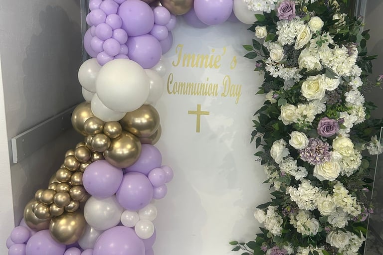 Elegant lavender, gold, and white balloon arch with floral garland for a first communion celebration.