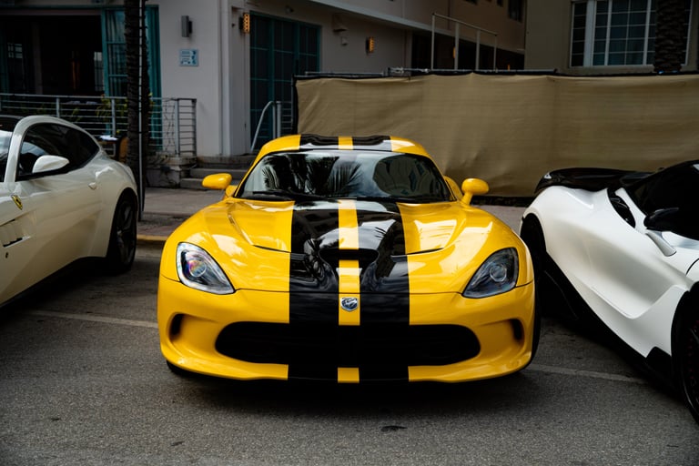 Yellow Dodge Viper with black racing stripes parked between luxury white sports cars on a city street.