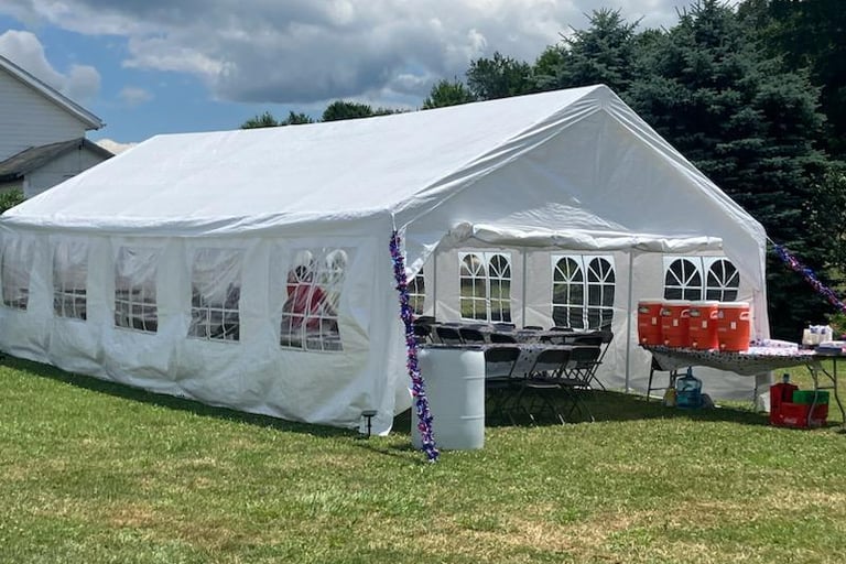 A large white event tent with windows and tables set up for an outdoor garden party on a lawn.