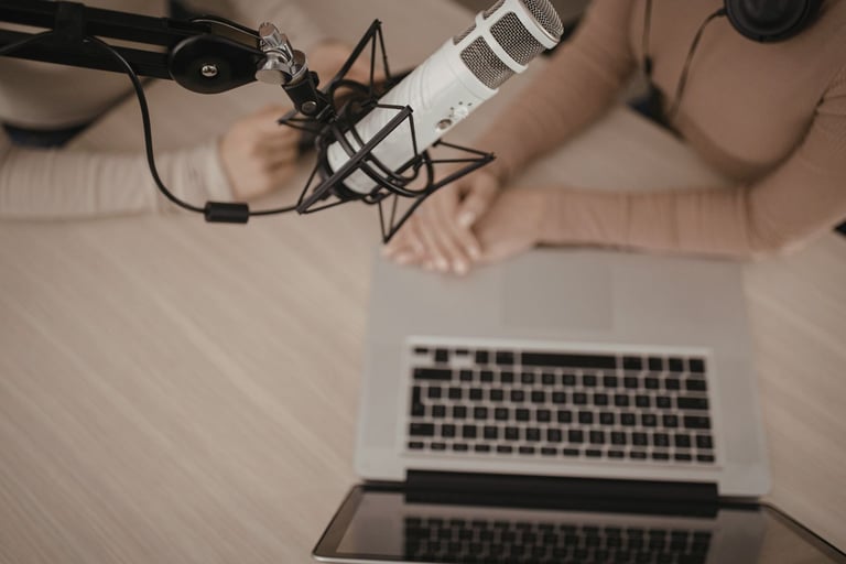 Professional condenser microphone in a podcast studio with two hosts using a laptop for recording.
