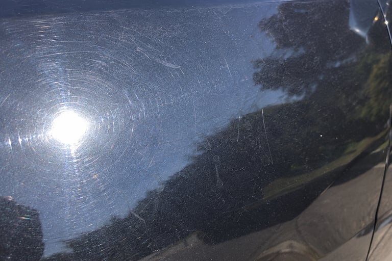 Close-up of swirl marks and light scratches on black car paint needing paint correction..