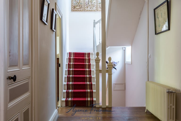 Élégant intérieur de maison avec escalier recouvert d’un tapis rouge, rampe blanche et parquet.