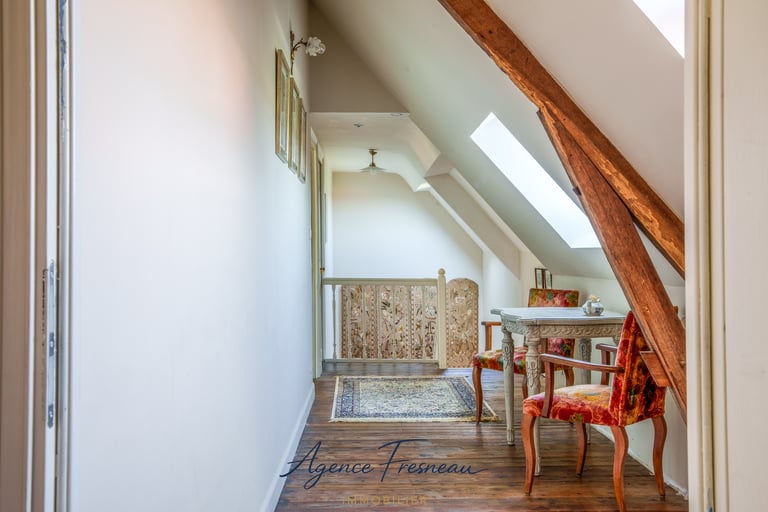 Couloir de combles lumineux avec poutres apparentes en bois, fenêtres de toit et petit espace repas 