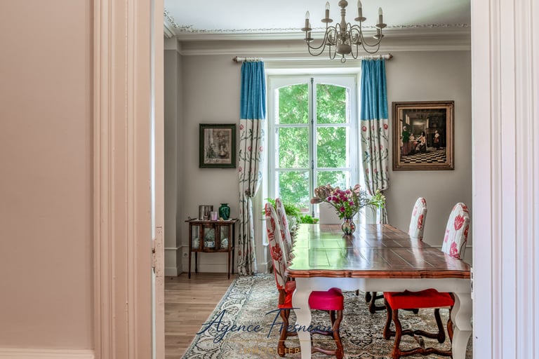 Élégante salle à manger avec table en bois, chaises à motifs floraux et rideaux bleus à proximité d’