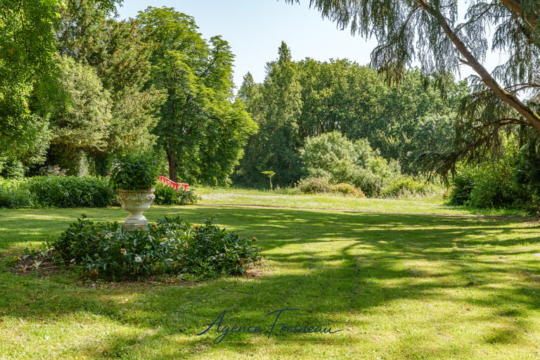 Urne de jardin en pierre dans un parc paysager, entourée de pelouse et de végétation.