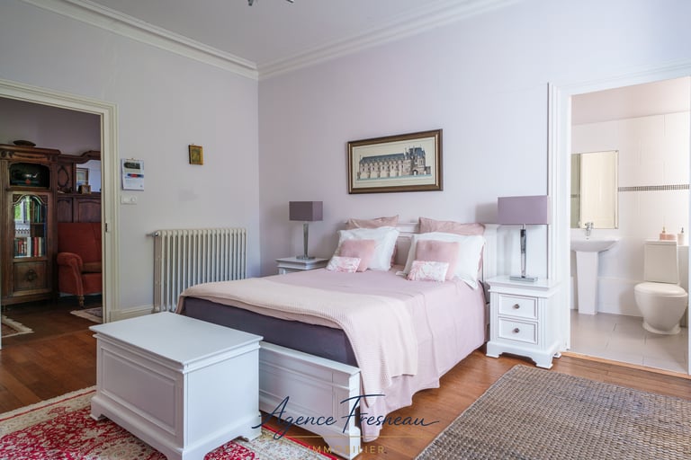 Élégante suite parentale avec linge de lit rose, mobilier blanc et salle de bains attenante