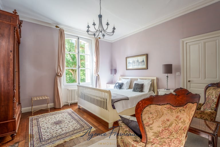 Élégante chambre de style campagne française avec lit en bois blanc, fauteuils vintage et lustre.