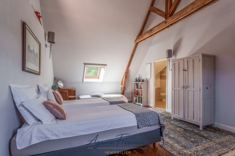 Chambre mansardée de style rustique avec poutres apparentes en bois et lits jumeaux.