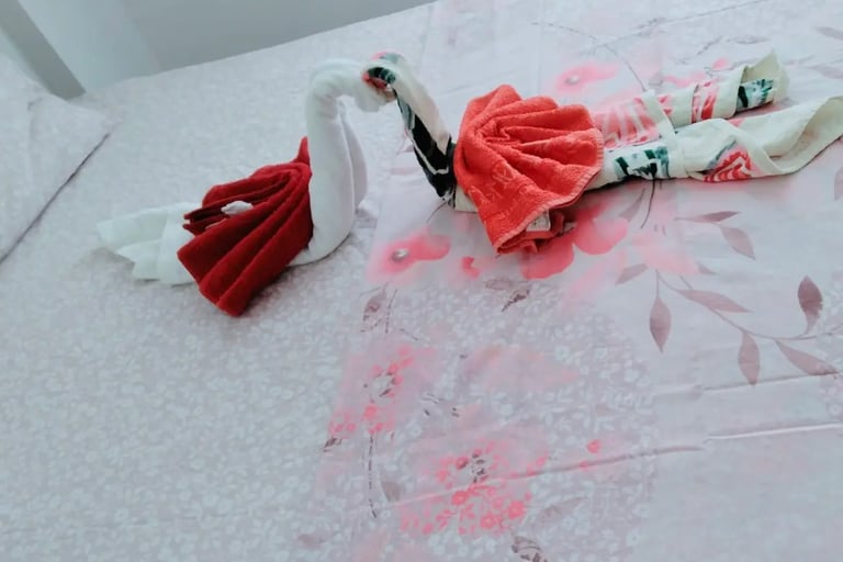Two decorative swan towels folded into a heart shape on a pink floral bedsheet in a hotel room.