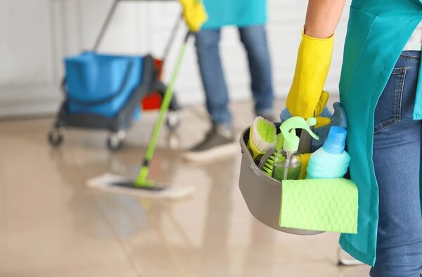 two people standing  one with mop and the other with cleaning supplies