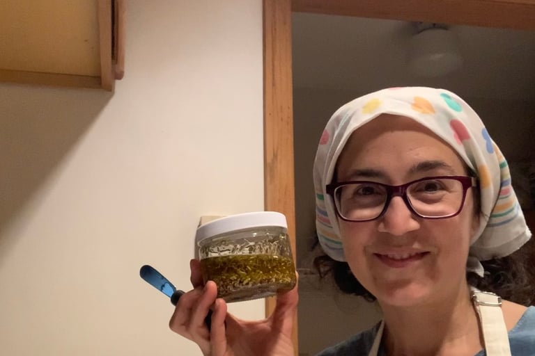 Katrina Matos with bandana covering hair, & holding up a jar of herb-infused oil