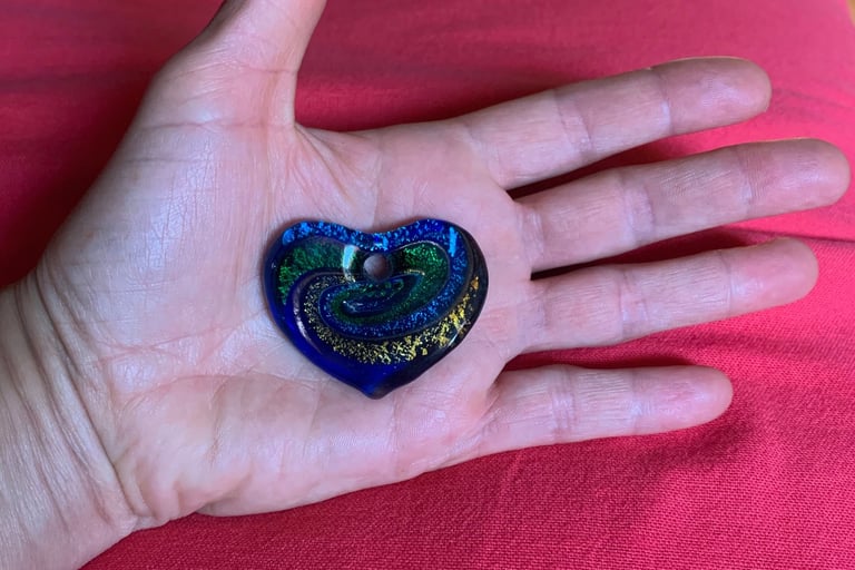 open hand with blue green 7 yellow glass heart on palm