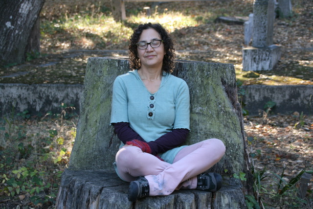 Katrina Matos sitting on tree trunk, slightly smiling, eyes closed