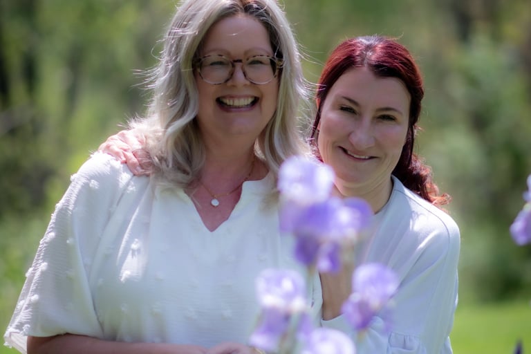 Two smiling women posing together outdoors behind purple iris flowers. sister_Athens_Ohio.jpg