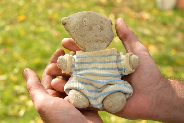 Doudou ancien en tissu, tenu dans des mains d’adulte, traces d’usure visibles