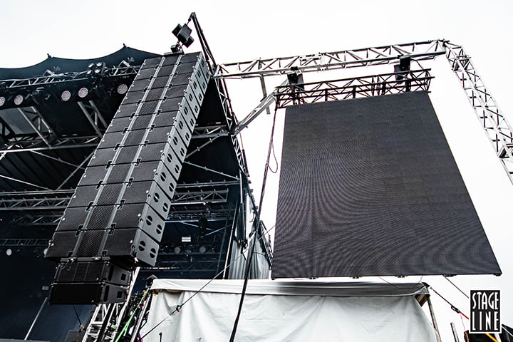 A large line array hanging from a mobile structure (Stageline) beside a LED Wall
