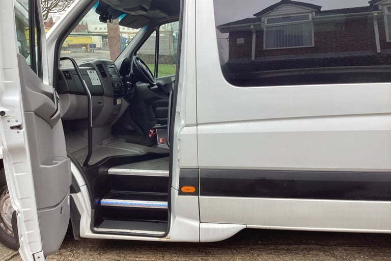 White passenger minibus with an open door showing the interior cabin and illuminated entry steps.