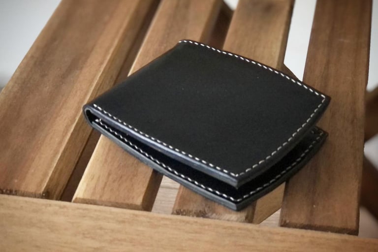 Handmade black leather wallet with white hand-stitched edges, resting on a wooden surface.