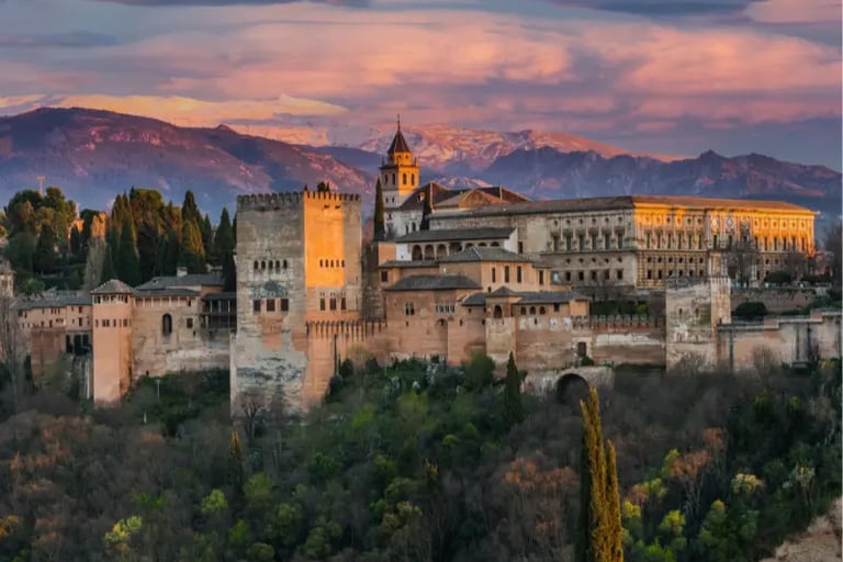Sunset view of the Alhambra palace and fortress complex in Granada with Sierra Nevada mountains.