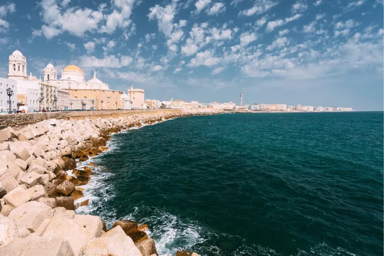 Panoramic view of the Cadiz Cathedral and rocky coastline against the blue Atlantic Ocean in Spain.