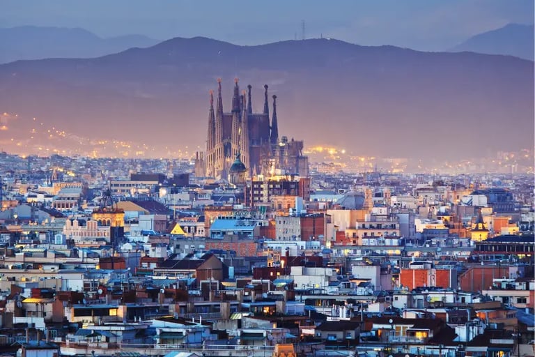 Barcelona city skyline at dusk featuring the Sagrada Familia basilica and misty mountains.