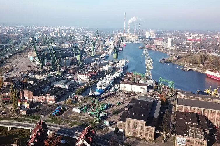 Aerial view of an industrial shipyard with large green cranes and ships along the city waterfront.