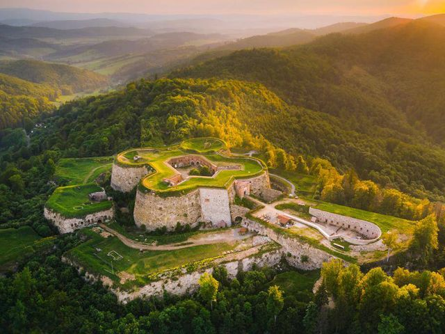 Aerial view of a historic star-shaped stone fortress nestled in lush green mountain hills at sunset.