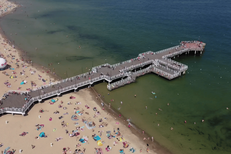Aerial view of a crowded sandy beach and wooden pier extending into the Baltic Sea.