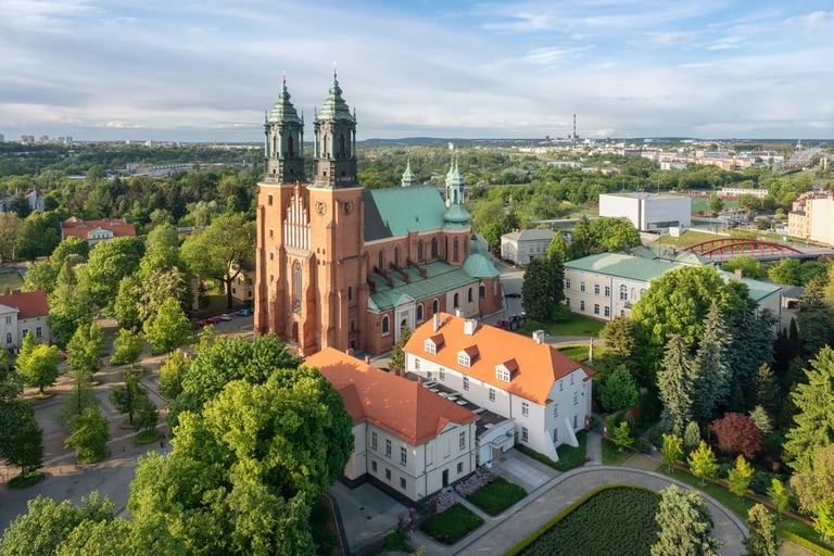 Aerial view of the brick Poznan Cathedral with twin towers and green roof in a lush city park.