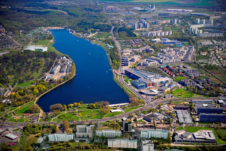 Aerial view of a blue city lake surrounded by green parks, urban buildings, and roads.