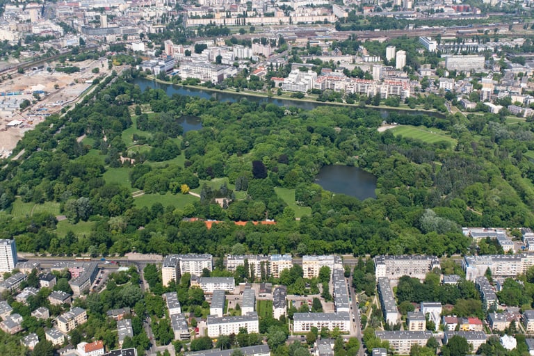 Aerial view of Skaryszewski Park in Warsaw featuring lush green trees, lakes, and surrounding city buildings.