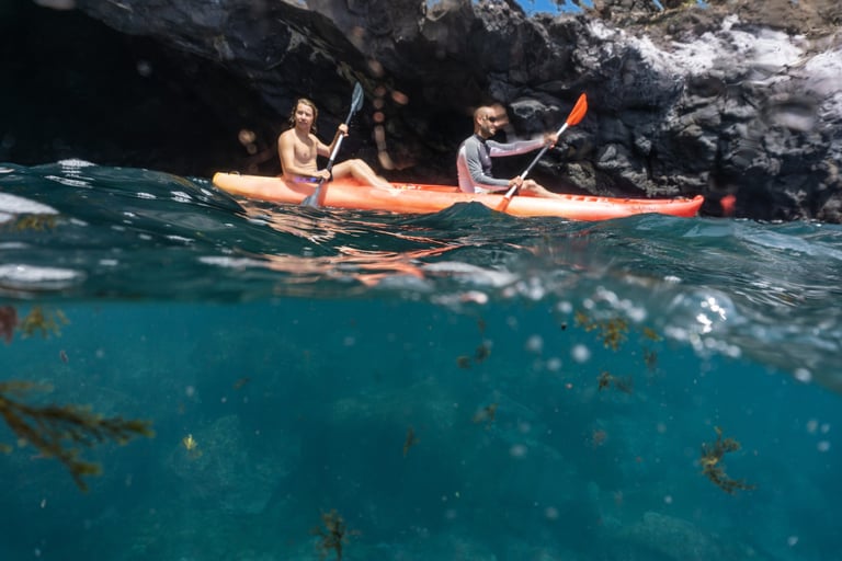 Two people kayaking inside a volcanic sea cave in Funchal, Madeira, with clear turquoise water below