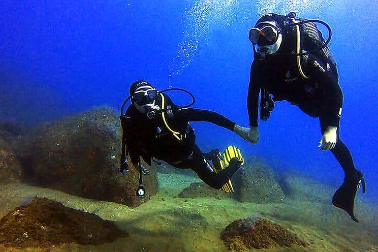 Two scuba divers exploring the underwater rocky seabed during an ocean dive in Funchal, Madeira