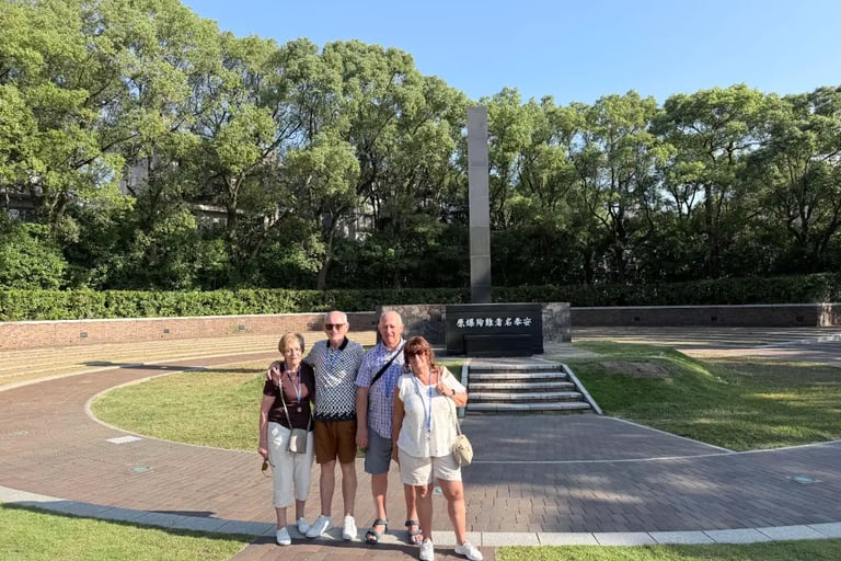 Four elderly travelers standing quietly in front of the atomic bomb hypocenter marker in Nagasaki