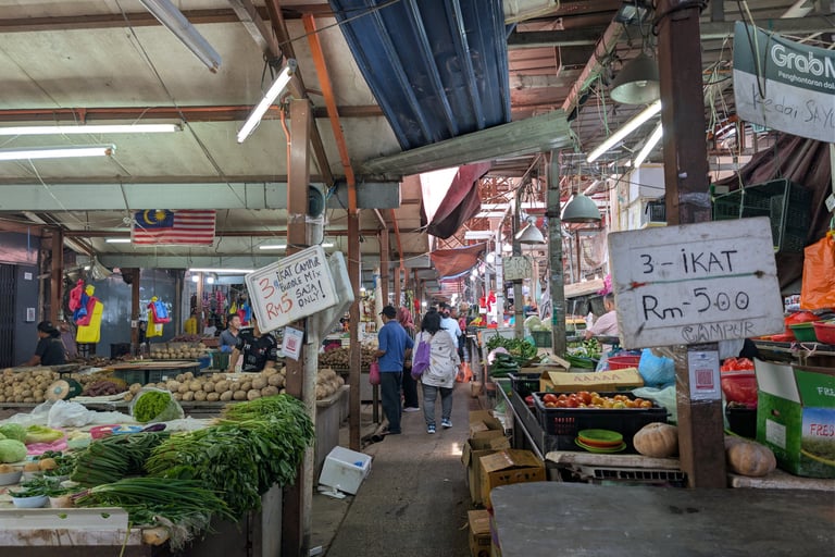 bustling Malaysian wet market with fresh vegetables, produce stalls, and shoppers under a canopy.