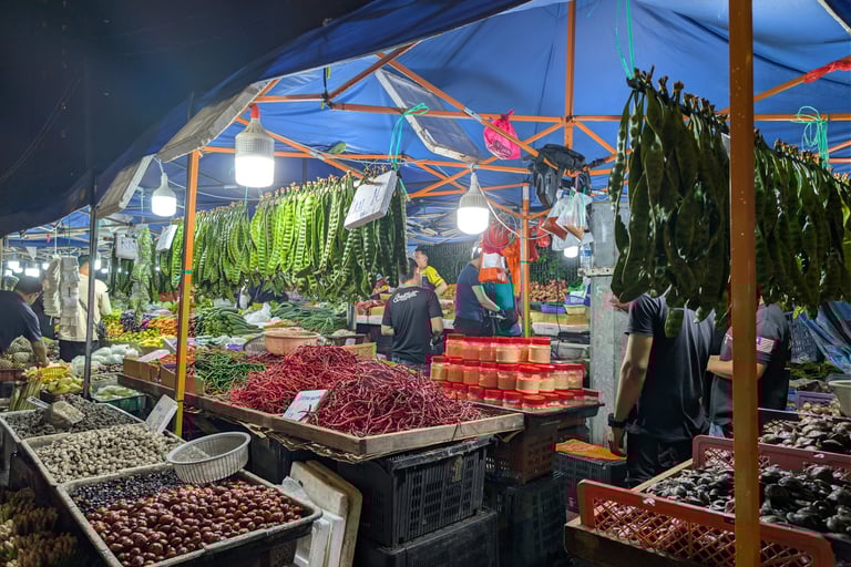 Night market stall in Malaysia selling fresh red chilies, stink beans, and local produce under a blue tent.