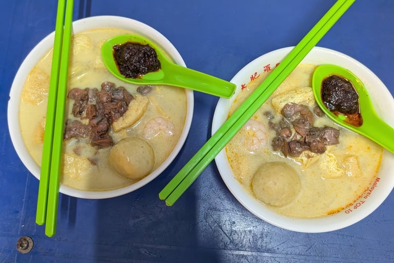 Two bowls of authentic Malaysian curry mee noodle soup with cockles, fish balls, and spicy sambal.
