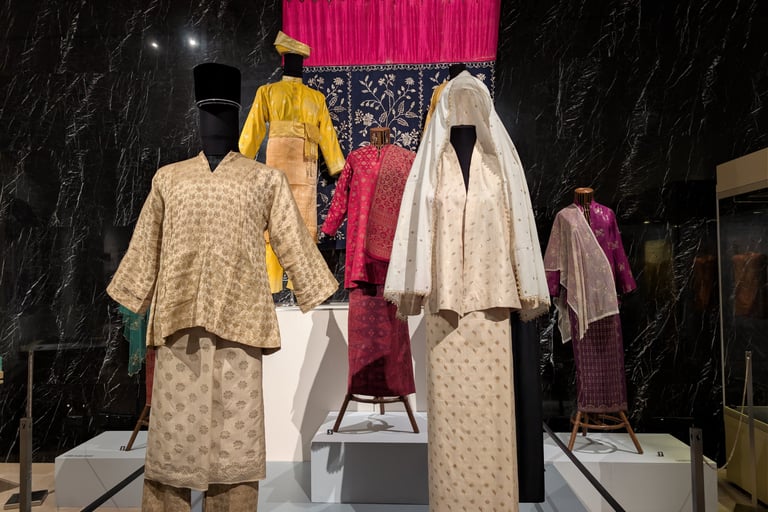 Traditional Malay Baju Kurung and Baju Melayu formal attire displayed on mannequins in a museum.