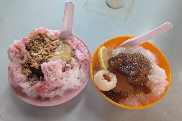 Two bowls of Malaysian lemon shaved ice and Ice Kacang desserts with peanuts and lychee.