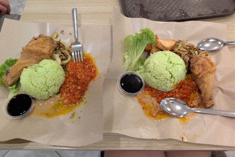Two plates of Malaysian Nasi Lemak with green rice, fried chicken, and spicy sambal sauce.