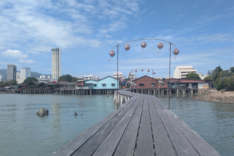 A wooden jetty at Jetty in Penang, Malaysia, with traditional stilt houses and the Komtar building in the distance.