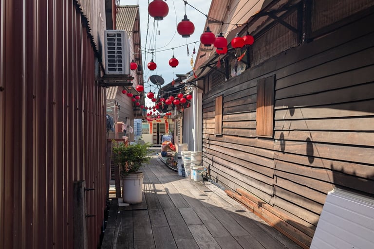 Red Chinese lanterns hanging over a narrow wooden boardwalk alley in a traditional village. Lim Jetty