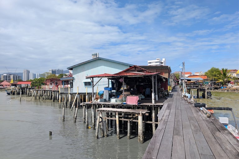 Traditional wooden stilt houses and jetties at the Lim Jetty of George Town, Penang, under a blue sky.