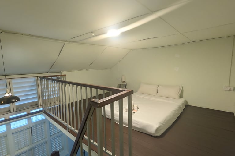 A loft bedroom with a white mattress on a dark wood floor and a metal railing overlooking the stairs