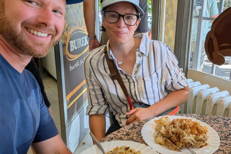 Moose and Bugs eating traditional Balkan burek pastry at an outdoor restaurant table.