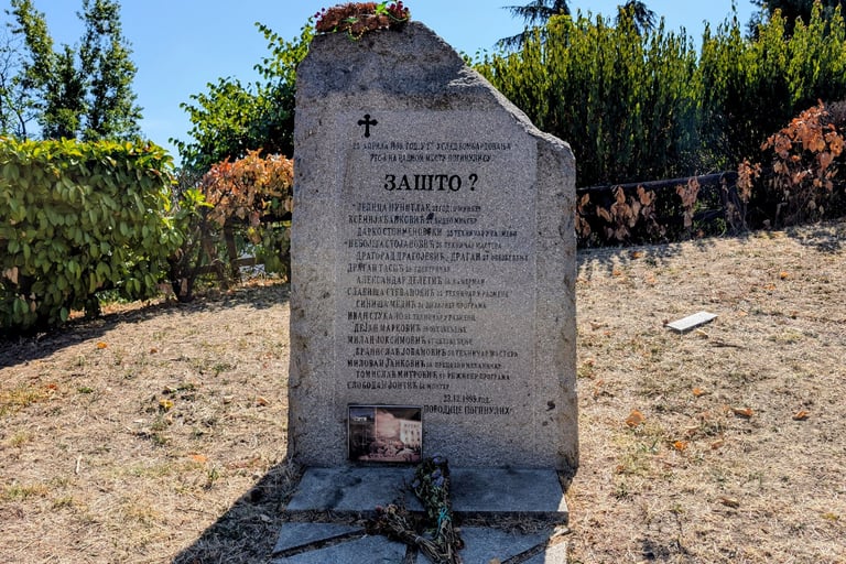 A stone memorial monument with Bulgarian inscriptions stands in a grassy park under a clear blue sky